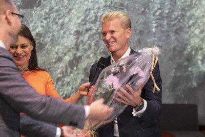 Hymyilevälle miehelle ojennetaan kukkakimppua.