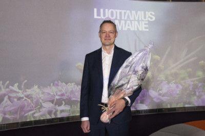 Kuva miehestä, jolla puku päällä ja kukkakimppu käsissä.
